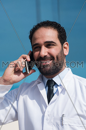 Young middle eastern doctor talking on the phone in front of a modern hospital