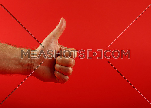 Man hand shoving thumb up ok good gesture over red background, side view