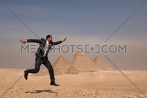 arabian business man jumping in desert with pyramids in background