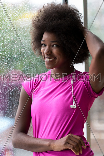 portrait of young afro american woman in gym on workout break while listening music on earphone  and dancing  rainy day and bad weather outdooor