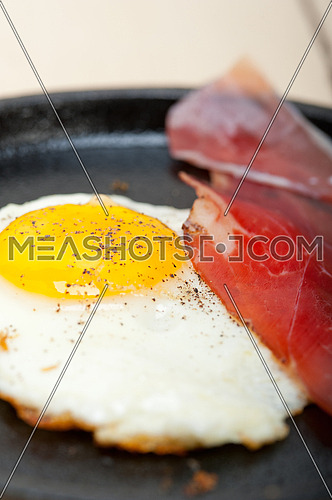 fried egg sunny side up with Italian tyrolean speck smoked ham on a skillet