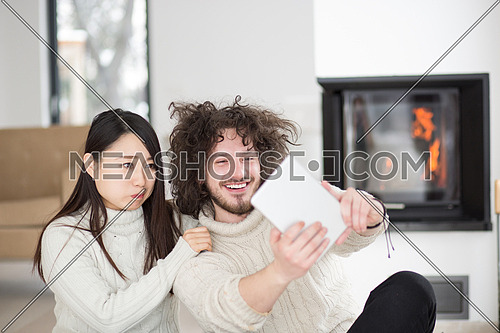 beautiful young multiethnic couple using tablet computer in front of fireplace on cold winter day at home