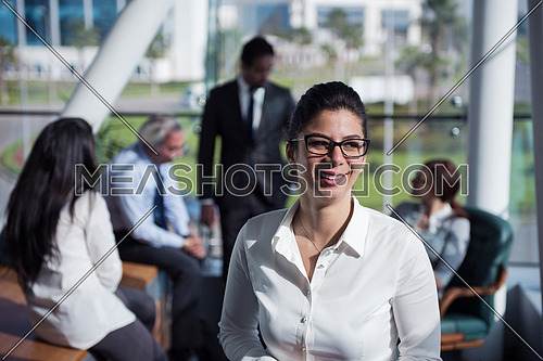 Portrait of a female executive wearing eye glasses and a group meeting is taking place at the background in a bright office