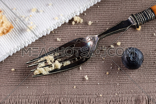 Fork in burlap with crumbs and a blueberry over brown burlap