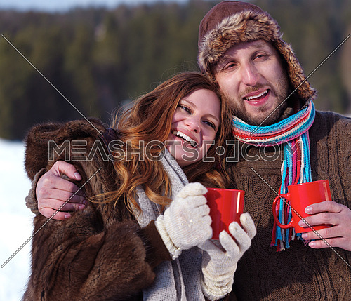 portrait of happy young couple outdoor on winter day drinking warm tea with fresh snow in background
