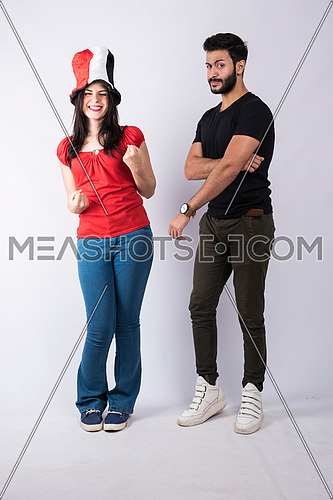 young couple standing and cheering, while the female wearing egyptian flag hat on white background