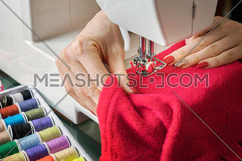 Young woman sewing fabric on sewing machine,sewing process in the phase of overstitchin,colored spools.