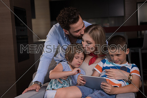 happy couple spending time with kids using tablet computer on an armchair  at home