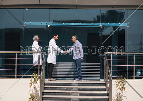 Smiling middle eastern doctor at the clinic giving an handshake to his patient, healthcare and professionalism concept