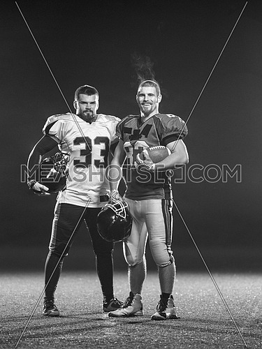 portrait of confident American football players holding ball while standing on field at night