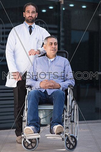 middle eastern sick man in a wheelchair and a young doctor in front of a large modern hospital