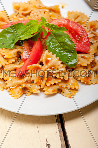 Italian pasta farfalle butterfly bow-tie with tomato basil sauce over white rustic wood table