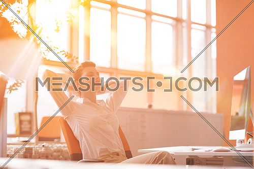 Happy young business woman relaxing and geting insiration while working on desktop computer at modern bright  starup office interior. Morning sunrise or sunset with sun flare in background.
