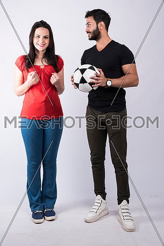 young couple standing and cheering on white background, while both of them having fun with a ball